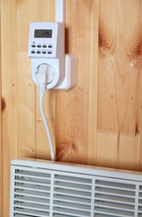 Working white electric convector heater plugged to timer power socket operated in smart house system against wooden wall inside room side view closeup