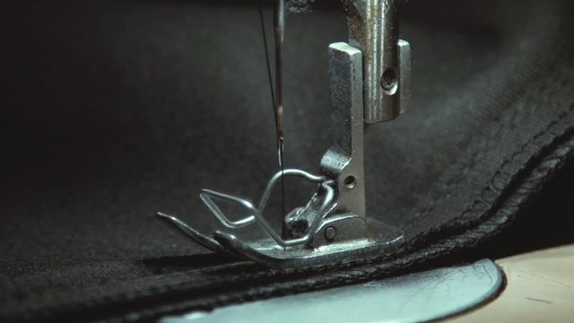 Macro. Panning on steel sewing needle in slow motion. Part of modern sewing machine isolated on black background. A hand of a dressmaker supporting a cloth while sewing on a sewing machine. Sewing.