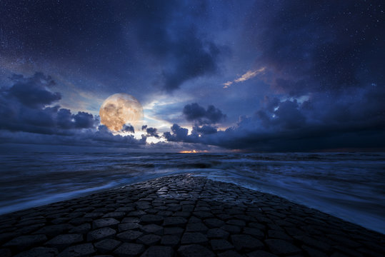 Fantastic stars and moon night over a stone road into the ocean