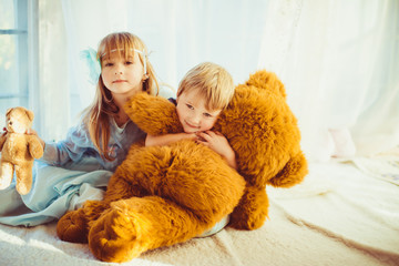 Nice child hugs soft large bear while lying behind his sister