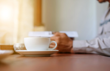 Man reading a book with white coffee cup front place.