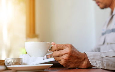 Man reading a book with white coffee cup in hand.
