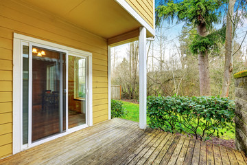 Empty wooden walkout deck, backyard view of yellow house