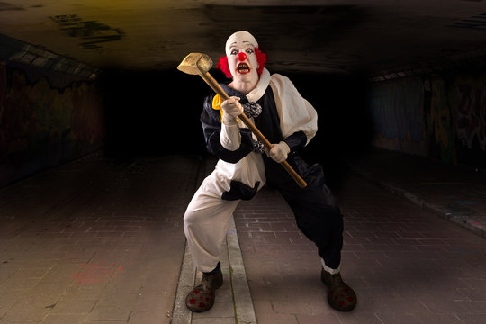 scary clown with a hammer standing in a tunnel
