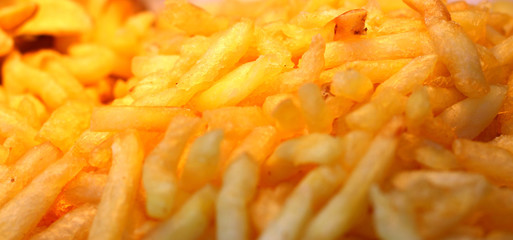 Large pan of fast food cooked sweet potato fries, fresh out of frying oil yellow colorful close up patterns