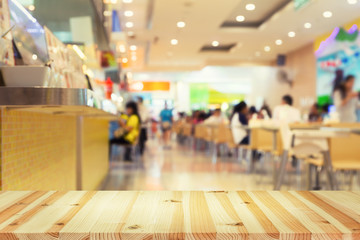 Defocused or blurred photo of food court montage with wood table top use for background.