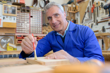 portrait of happy senior carpenter varnishing wood in workshop