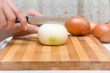 Obraz na płótnie Canvas Woman's hand with a knife cuts the onion on the wooden board in the kitchen. Healthy eating and lifestyle.