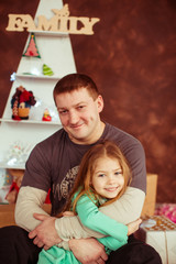 Fototapeta premium Dreamy little girl lies on father's arms before a red wall