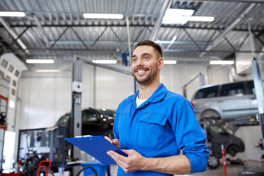 happy mechanic man with clipboard at car workshop