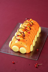 Contemporary Christmas Yule Log Cake covered with orange glaze and decorated with french macarons and chocolate loops, on burgundy background. 