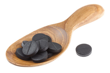 Active black charcoal pills on woodne spoon isolated on white background