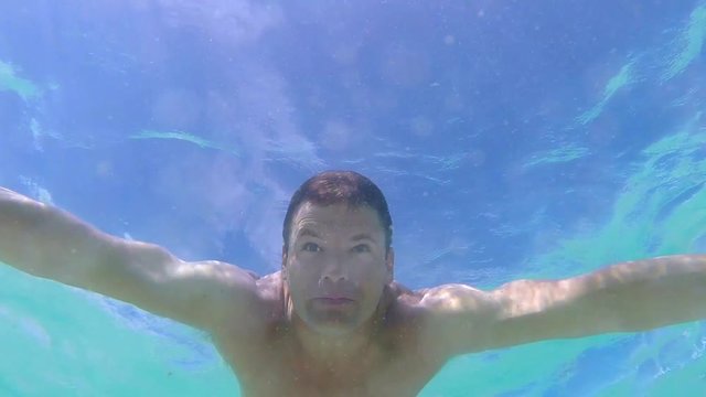 Slow motion 60 fps underwater low angle shot of muscular Caucasian man swimming breast stroke with eyes open under surface of sea