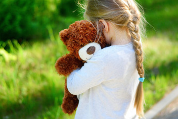 Adorable sad girl with teddy bear in park.