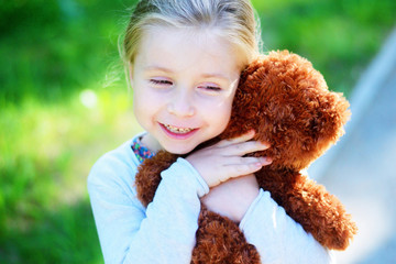 Adorable little girl with teddy bear in park.