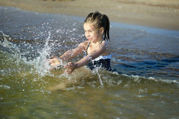 Adorable little girl is splashing and smashing sea water and having fun