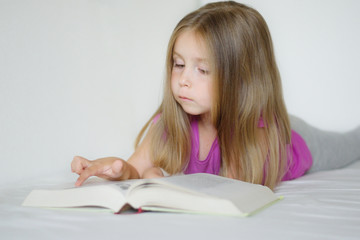 Adorable little girl lying on the bed and reading a book