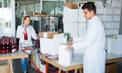 professional male employee in coat packing bottles into carton p