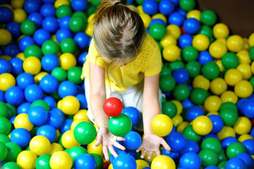 Fototapeta na wymiar Happy little girl playing at colorful plastic balls playground