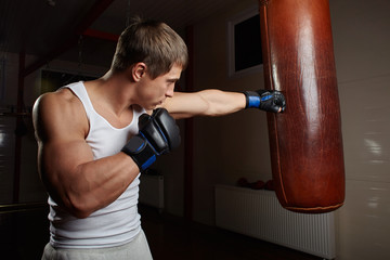 young muscular male boxer punch punching bag in gym interior