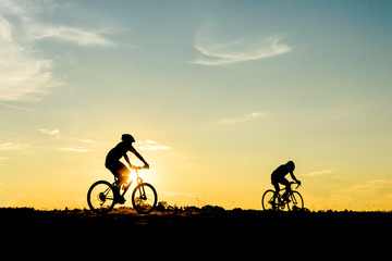 Obraz premium Silhouette of cyclist with friend motion on sunset background
