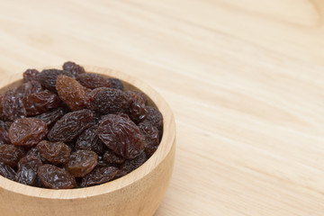 raisins in bowl on wooden table.