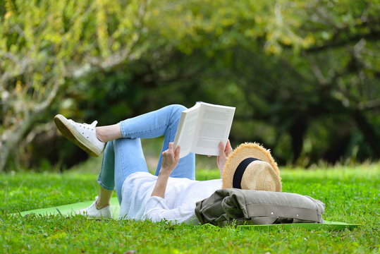 Happy woman lying on green grass reading a book in the park (outdoors)