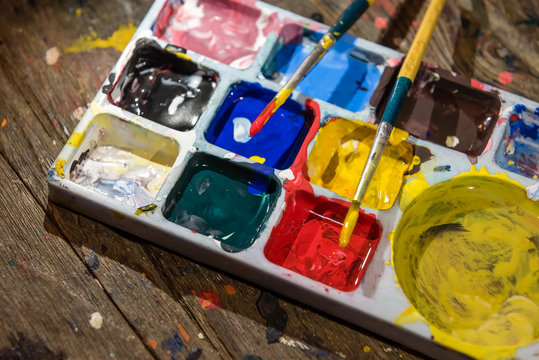 Colorful colors palette and paint brushes on dirty wooden artist table