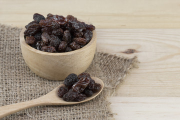 raisins in spoon with raisins in bowl on wooden table.