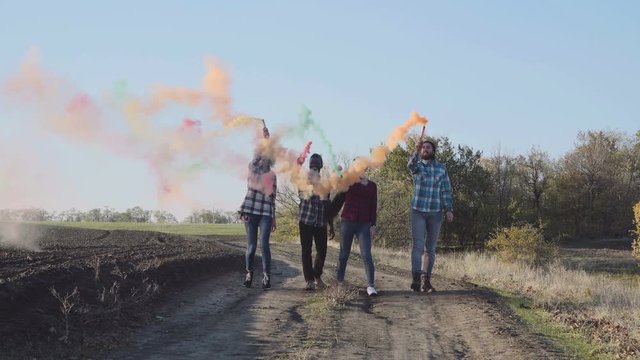 Four Happy Young Multi Racial Friends In Rural Road Under Blue Sky With Colored Smoke Grenades.