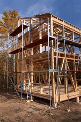 Metal scaffolding around the unfinished house.  Construction of ecological house. Wooden frame of house under construction.Framed New Construction of a House. Timber house in building process
