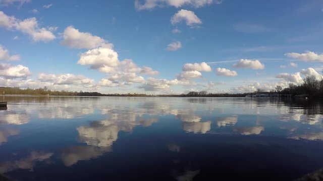 Patches of clouds travelling through the sky and their reflection in a lake, time lapse.