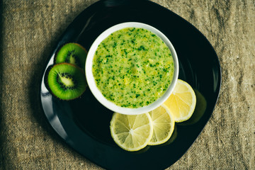 green smoothie with lemon and kiwi fruit on black plate. Burlap texture