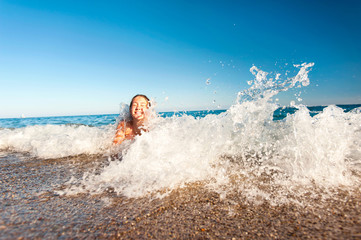 Happy young girl enjoying in sea splashing waves. Mediterranean