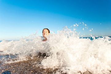 Happy young girl enjoying in sea splashing waves. Mediterranean