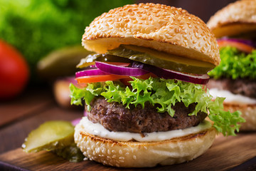 Big sandwich - hamburger burger with beef, pickles, tomato and tartar sauce on wooden background.