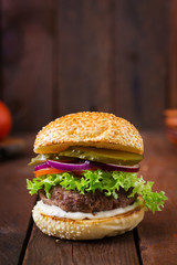 Big sandwich - hamburger burger with beef, pickles, tomato and tartar sauce on wooden background.