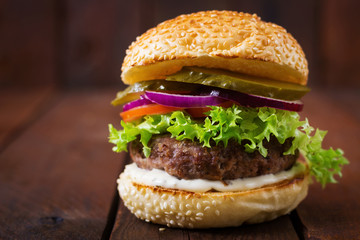 Big sandwich - hamburger burger with beef, pickles, tomato and tartar sauce on wooden background.