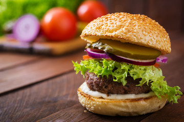 Big sandwich - hamburger burger with beef, pickles, tomato and tartar sauce on wooden background.