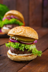 Big sandwich - hamburger burger with beef, pickles, tomato and tartar sauce on wooden background.
