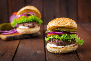 Big sandwich - hamburger burger with beef, pickles, tomato and tartar sauce on wooden background.