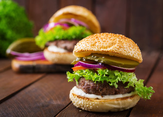 Big sandwich - hamburger burger with beef, pickles, tomato and tartar sauce on wooden background.