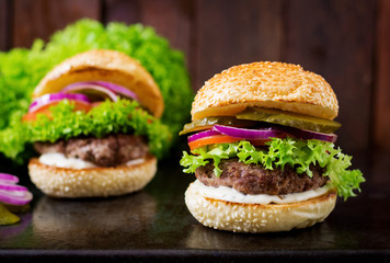 Big sandwich - hamburger burger with beef, pickles, tomato and tartar sauce on black background.