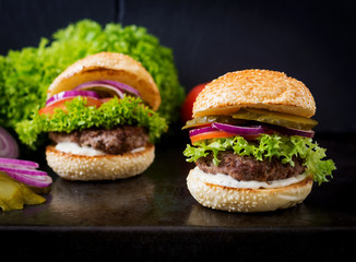 Big sandwich - hamburger burger with beef, pickles, tomato and tartar sauce on black background.