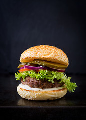 Big sandwich - hamburger burger with beef, pickles, tomato and tartar sauce on black background. - obrazy, fototapety, plakaty