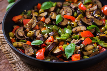 Hot spicy stew eggplant, sweet pepper, olives and capers with basil leaves.