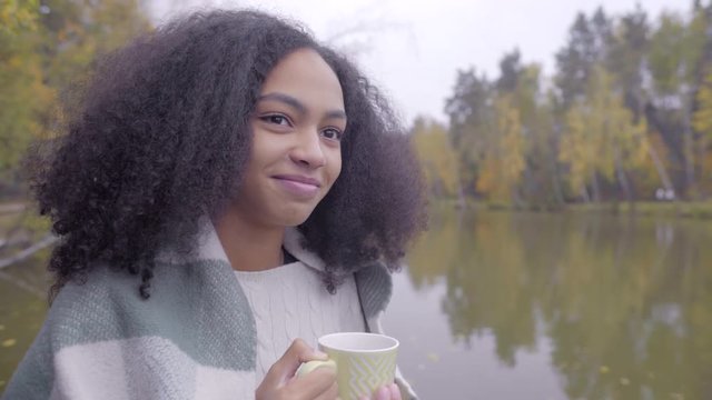 Cute black girl wrapping herself in woolen plaid and drinking hot tea