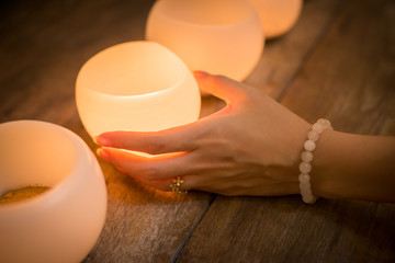 Candle in young woman hands on wooden background