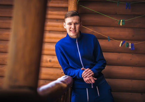 blond man in a blue sports suit on the background of wooden wall