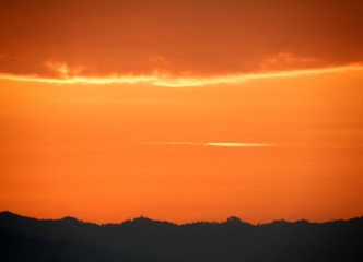 Orange gradation of sunset cloudy sky over the silhouette of mountain range, Thailand